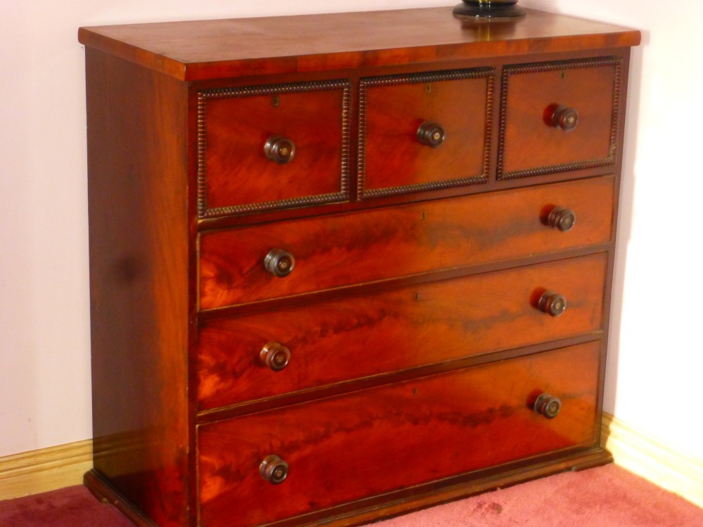 A Regency period flame mahogany chest of drawers featuring three small upper drawers above three long graduating drawers with turned wooden knobs.