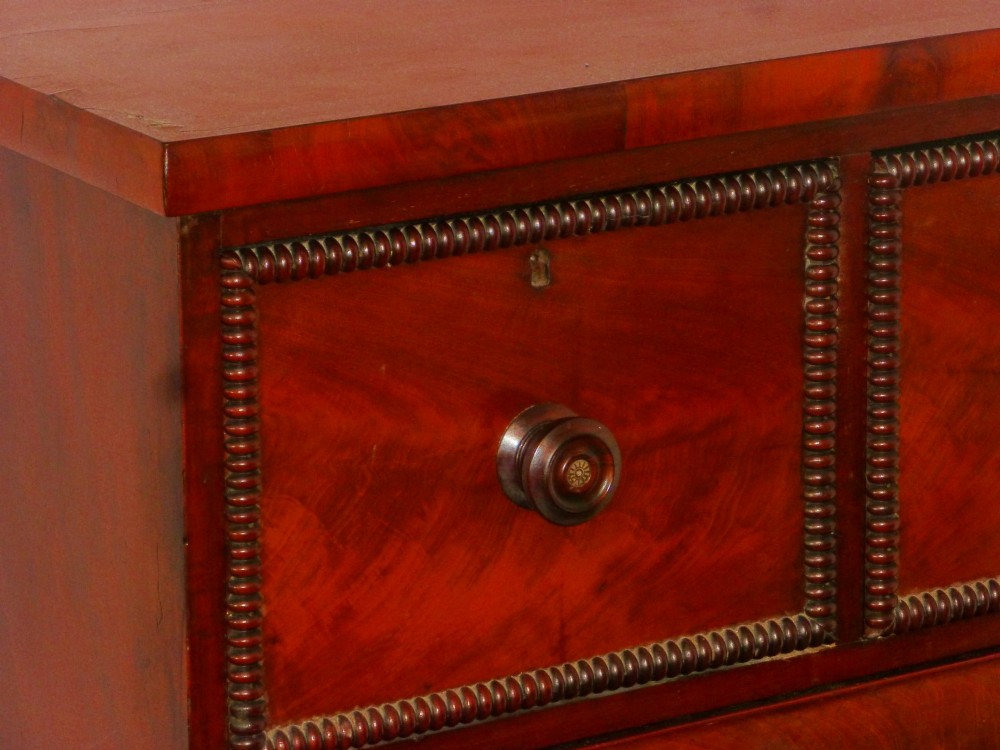 A Regency period flame mahogany chest of drawers featuring three small upper drawers above three long graduating drawers with turned wooden knobs. View II