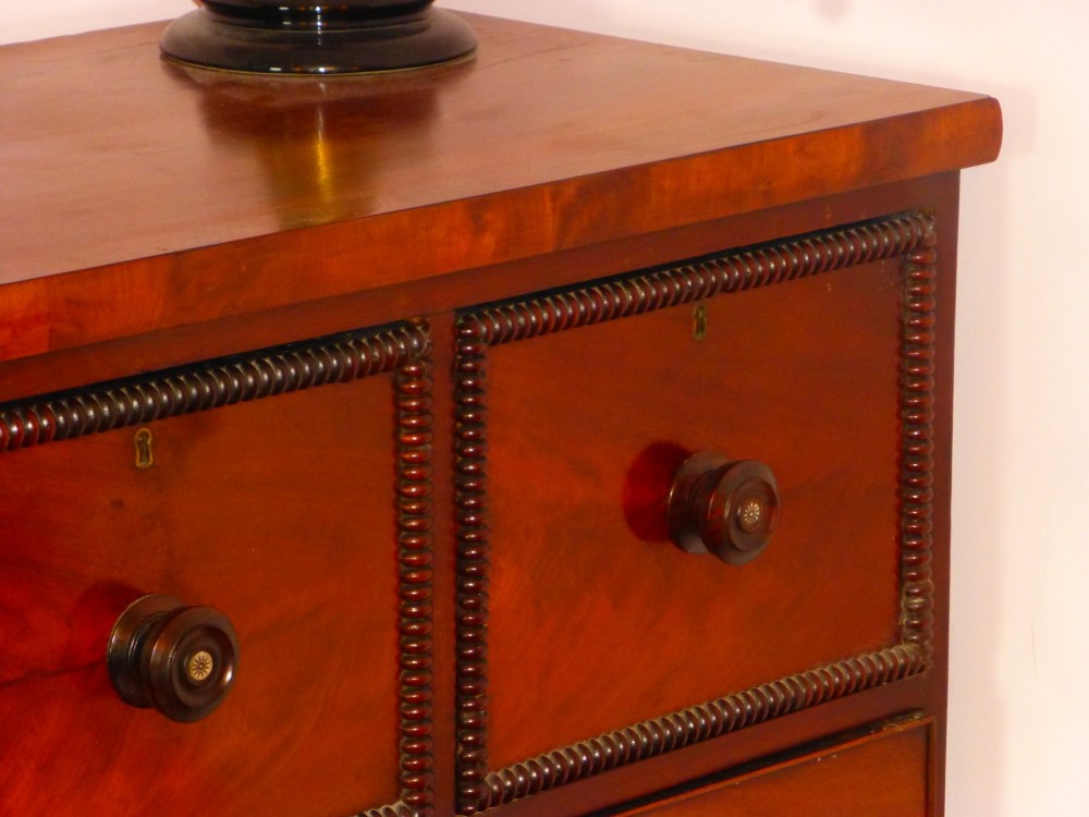 A Regency period flame mahogany chest of drawers featuring three small upper drawers above three long graduating drawers with turned wooden knobs. View III