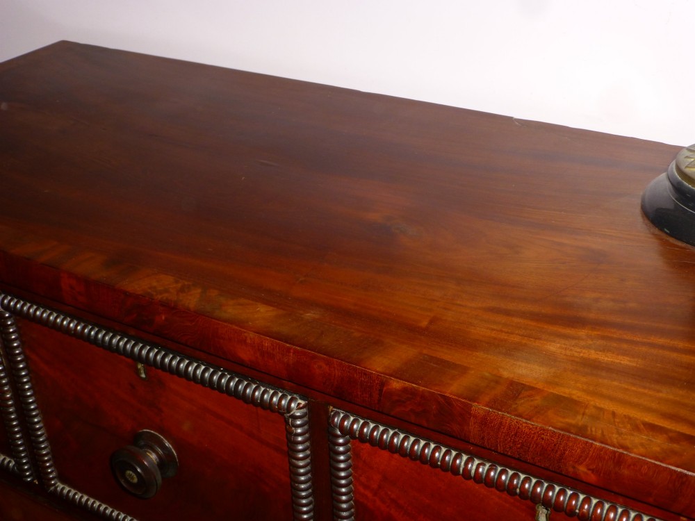 A Regency period flame mahogany chest of drawers featuring three small upper drawers above three long graduating drawers with turned wooden knobs. View IV