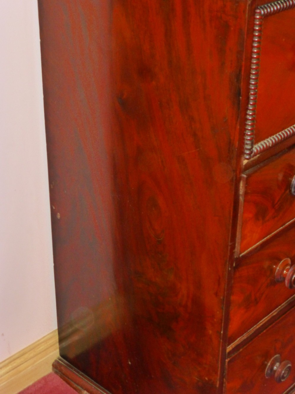 A Regency period flame mahogany chest of drawers featuring three small upper drawers above three long graduating drawers with turned wooden knobs. View V