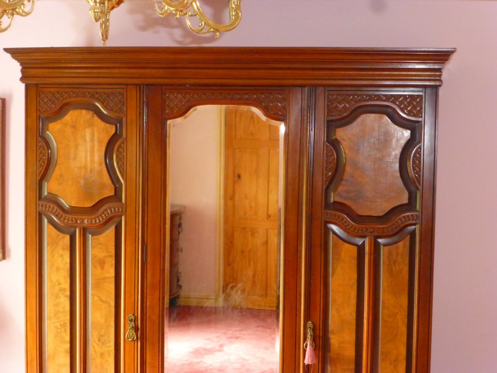 A mid-19th-century Victorian triple wardrobe made of rich burr walnut, featuring a central full-length mirror door flanked by two carved panelled doors. View VI