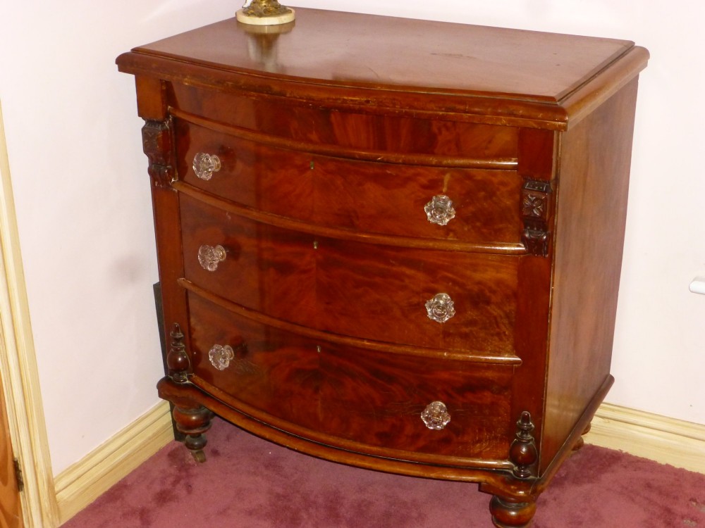 Victorian mahogany bowfront chest of drawers featuring three graduated drawers with clear glass handles and carved side pilasters.