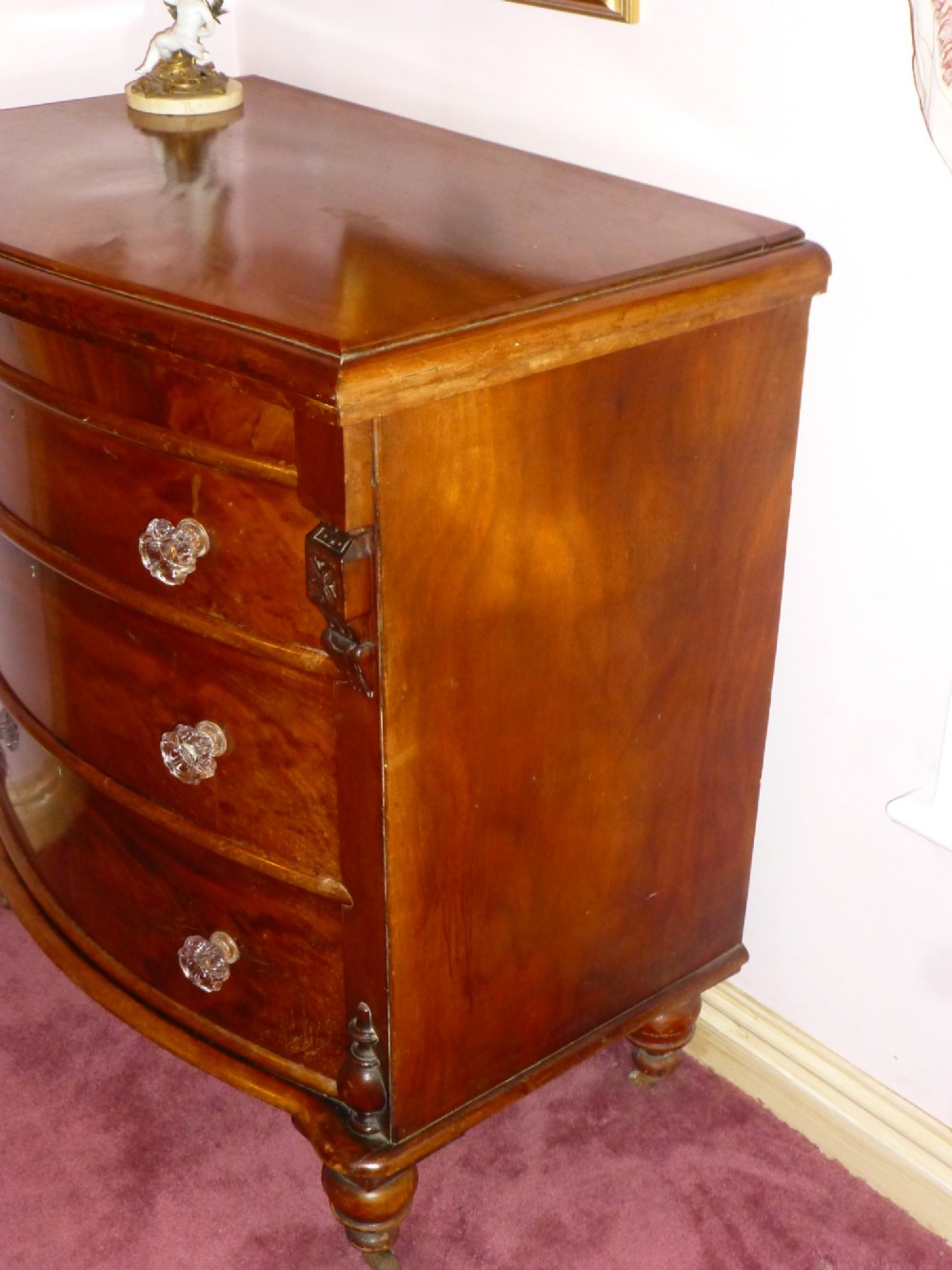 Victorian mahogany bowfront chest of drawers featuring three graduated drawers with clear glass handles and carved side pilasters. View II