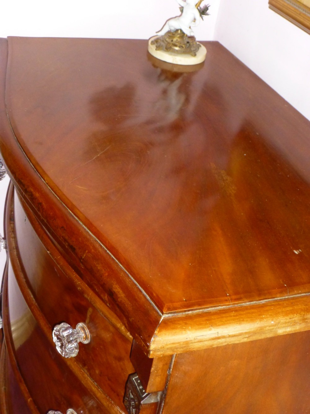 Victorian mahogany bowfront chest of drawers featuring three graduated drawers with clear glass handles and carved side pilasters. View III