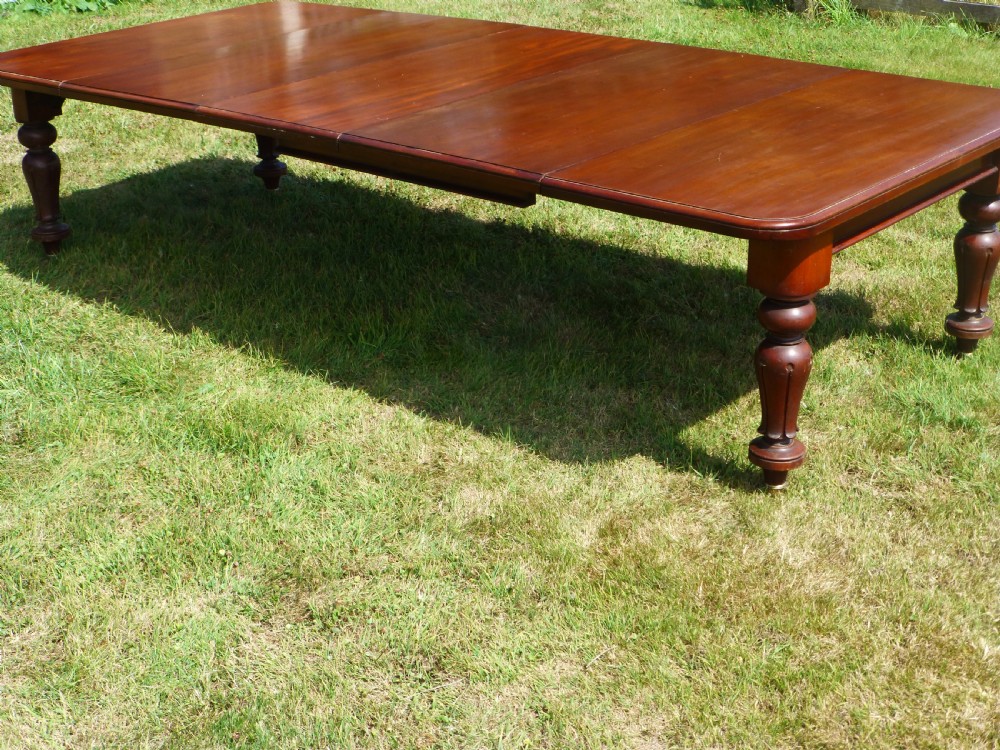 A large Regency extending mahogany dining table featuring a polished rectangular top, three extension leaves, and turned wood legs. View II