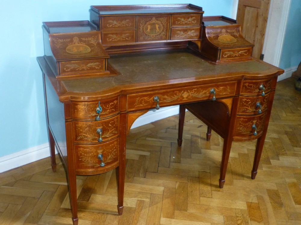 An Edwardian mahogany Carlton House desk featuring intricate floral marquetry inlay, a leather writing surface, and a curved raised tier of drawers.