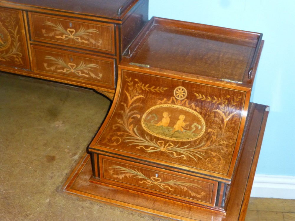 An Edwardian mahogany Carlton House desk featuring intricate floral marquetry inlay, a leather writing surface, and a curved raised tier of drawers. View II