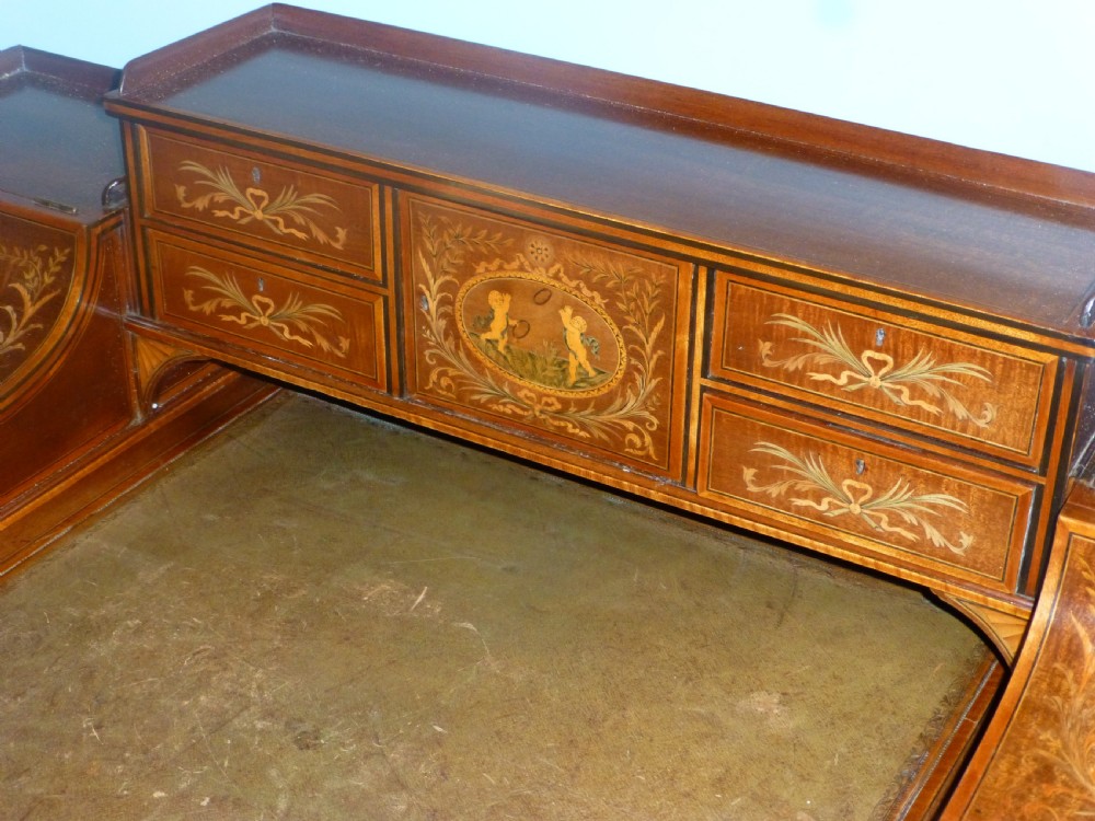 An Edwardian mahogany Carlton House desk featuring intricate floral marquetry inlay, a leather writing surface, and a curved raised tier of drawers. View III