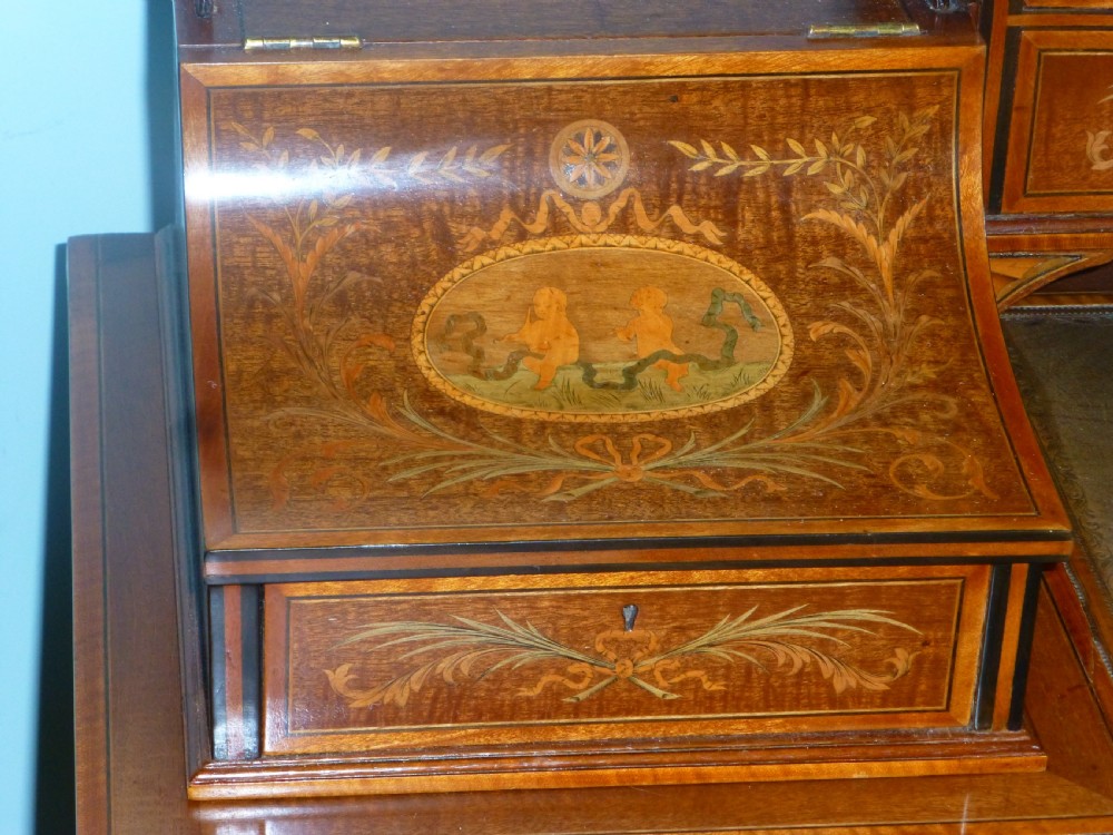 An Edwardian mahogany Carlton House desk featuring intricate floral marquetry inlay, a leather writing surface, and a curved raised tier of drawers. View V