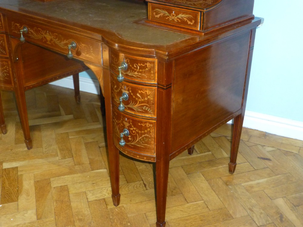 An Edwardian mahogany Carlton House desk featuring intricate floral marquetry inlay, a leather writing surface, and a curved raised tier of drawers. View VI