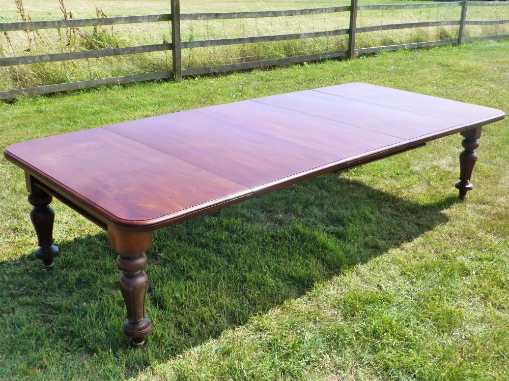 A large mahogany wind-out extending dining table featuring turned legs fitted with brass castors and rounded top corners. View VI