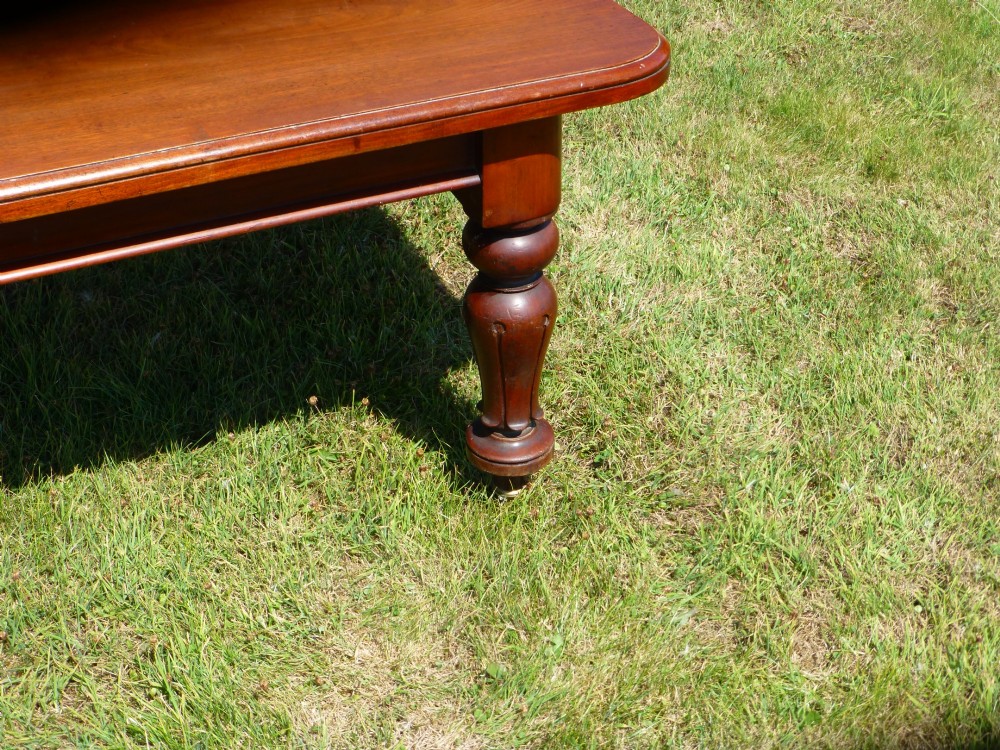 A large mahogany wind-out extending dining table featuring turned legs fitted with brass castors and rounded top corners. View XI