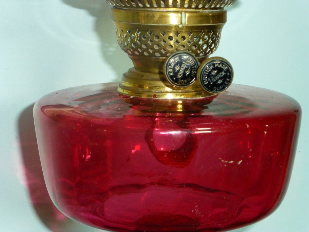 A Victorian cranberry glass and brass duplex oil lamp featuring a fluted column base, red glass reservoir, and a ruffled etched shade. View V