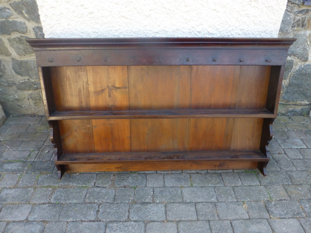 An 18th-century dark oak delft plate rack featuring two wide display shelves, a planked backboard, a moulded cornice, and metal cup hooks along the top rail.