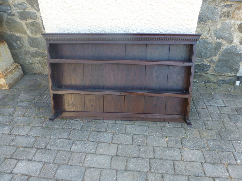 An 18th-century Georgian dark oak delft plate rack featuring three horizontal open display shelves and a dentil moulded top cornice.