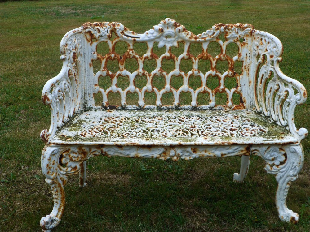 A Victorian white painted cast iron garden bench displaying an ornate latticework backrest, scrolled armrests, pierced seat pattern, and areas of rust patination. View II