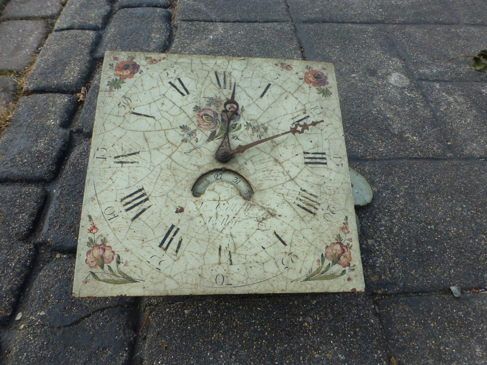 A square off-white painted longcase clock dial from the late 18th century featuring hand-painted floral corners, Roman numerals, steel hands, and surface crazing. View II