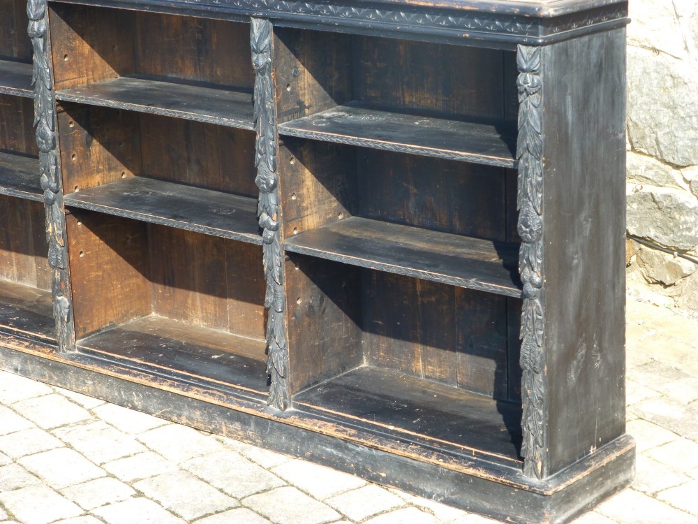 A low ebonised oak open bookcase featuring three bays with adjustable shelves and carved upright stiles. View II