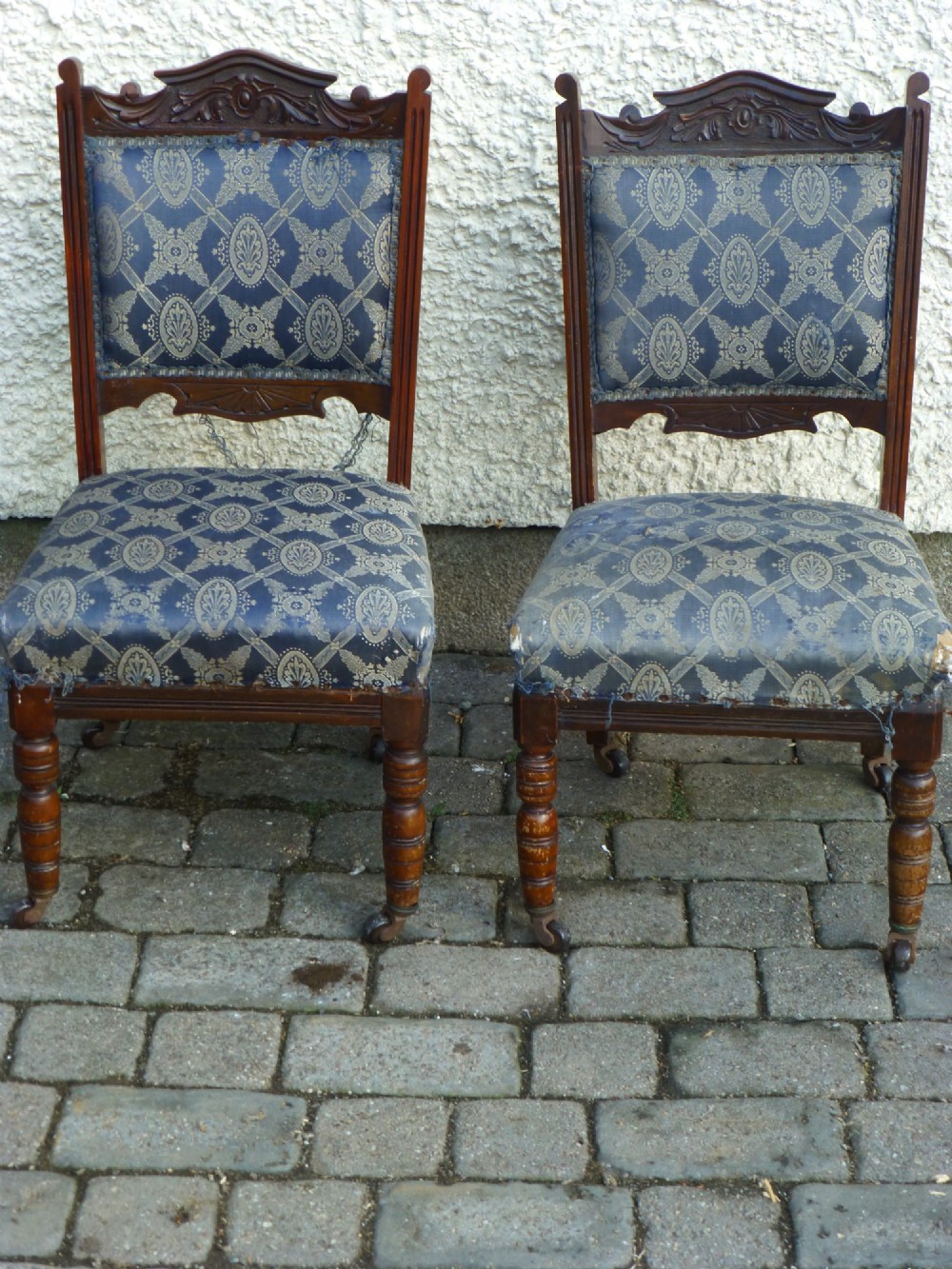 A pair of 19th-century Victorian carved walnut nursing chairs with low seats, turned front legs on castors, and worn blue patterned fabric.