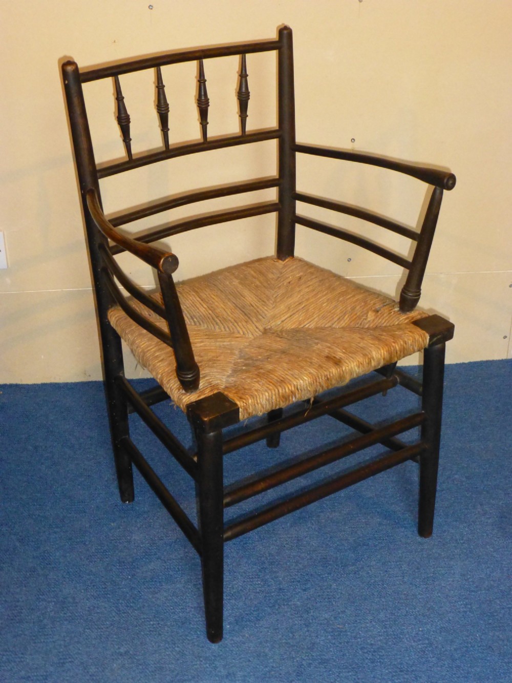 An Arts and Crafts ebonised wooden armchair featuring turned back spindles, curved armrests, and a woven rush seat.
