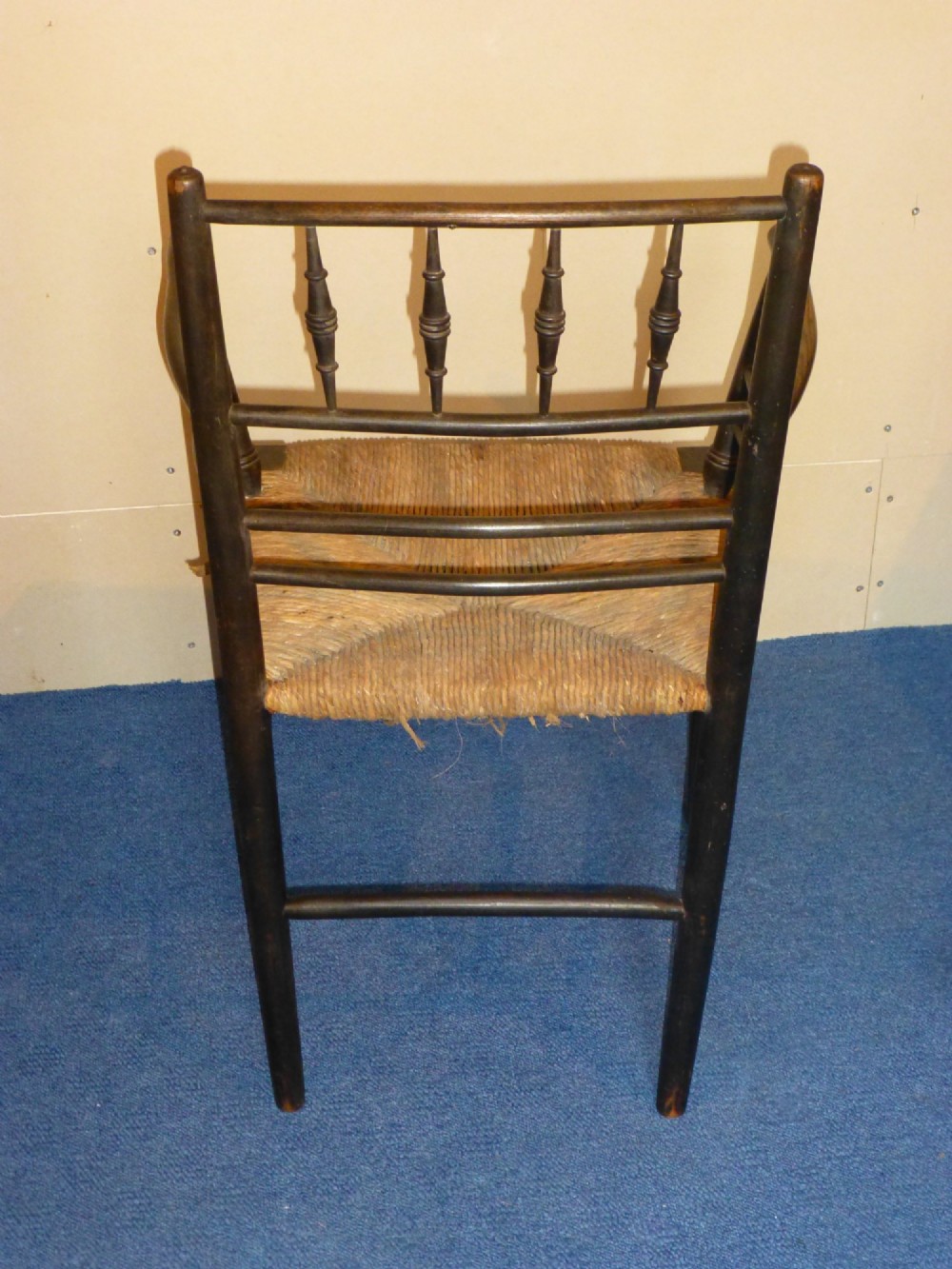 An Arts and Crafts ebonised wooden armchair featuring turned back spindles, curved armrests, and a woven rush seat. View IV