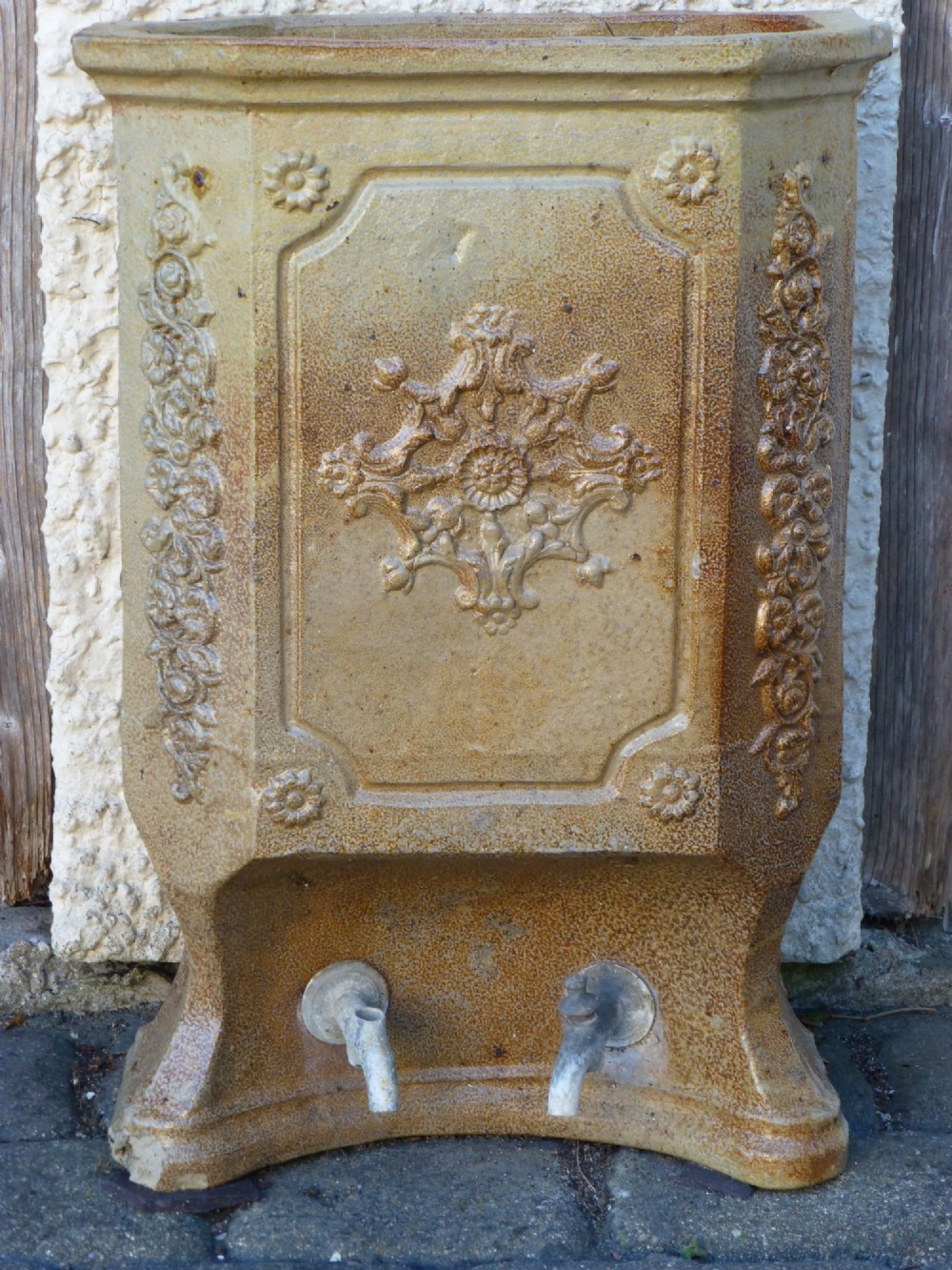 A 19th-century French salt-glazed stoneware water filter fountain in ochre brown with ornate floral relief carvings and twin brass spigots at the base.