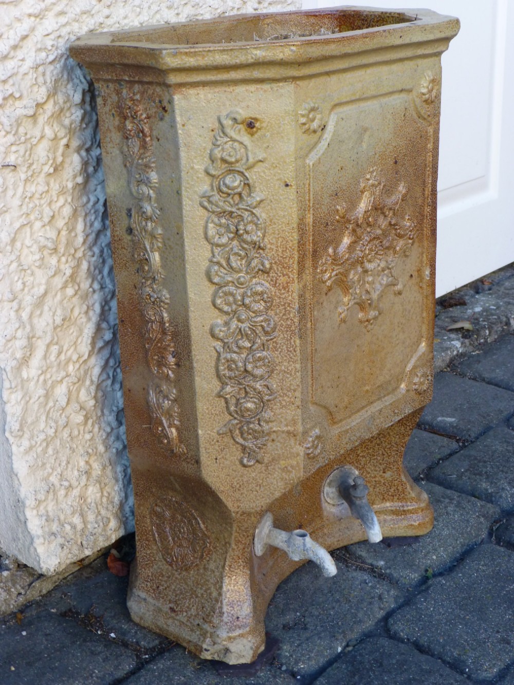 A 19th-century French salt-glazed stoneware water filter fountain in ochre brown with ornate floral relief carvings and twin brass spigots at the base. View II