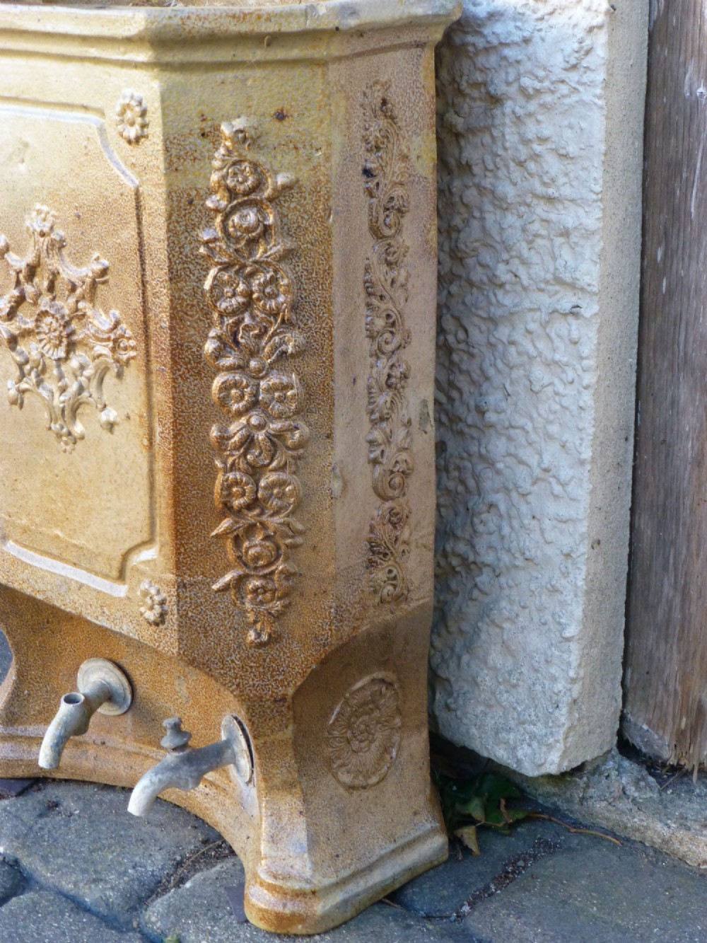 A 19th-century French salt-glazed stoneware water filter fountain in ochre brown with ornate floral relief carvings and twin brass spigots at the base. View III