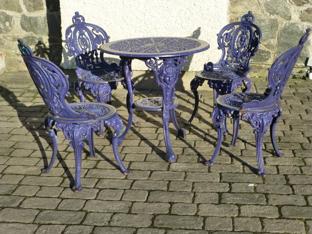 A nineteenth-century painted purple cast iron garden suite consisting of a round openwork table and four matching ornate medallion chairs.