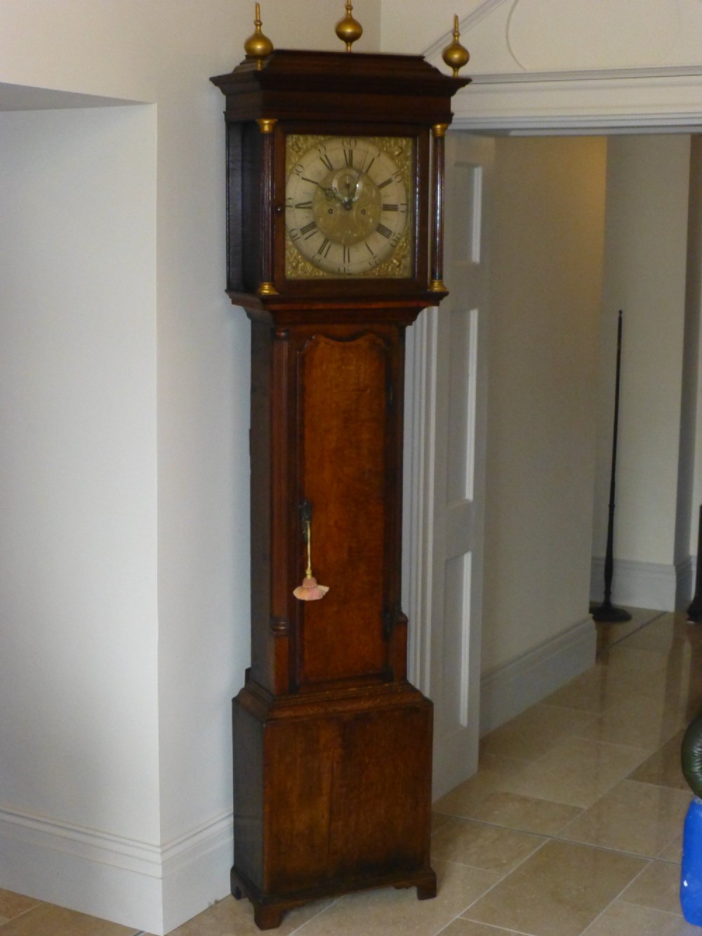 An eighteenth-century oak and walnut longcase clock featuring a square brass dial, decorative brass finials, and a slender veneered trunk door.