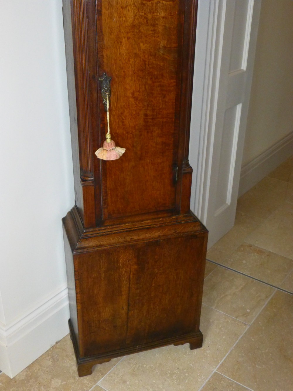 An eighteenth-century oak and walnut longcase clock featuring a square brass dial, decorative brass finials, and a slender veneered trunk door. View III