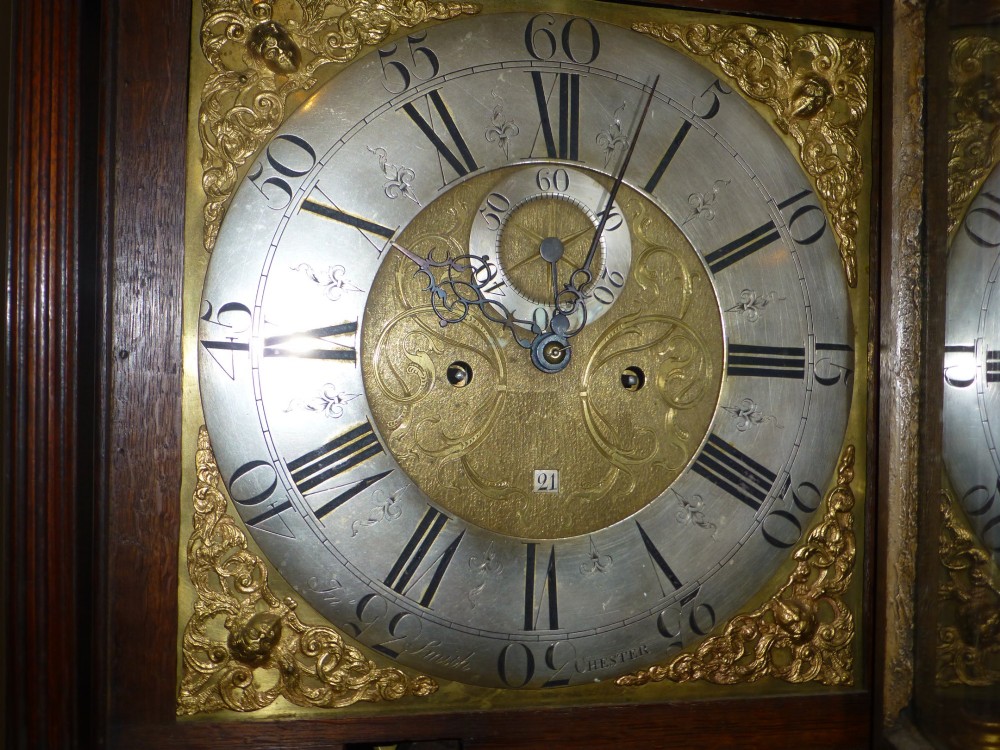 An eighteenth-century oak and walnut longcase clock featuring a square brass dial, decorative brass finials, and a slender veneered trunk door. View V