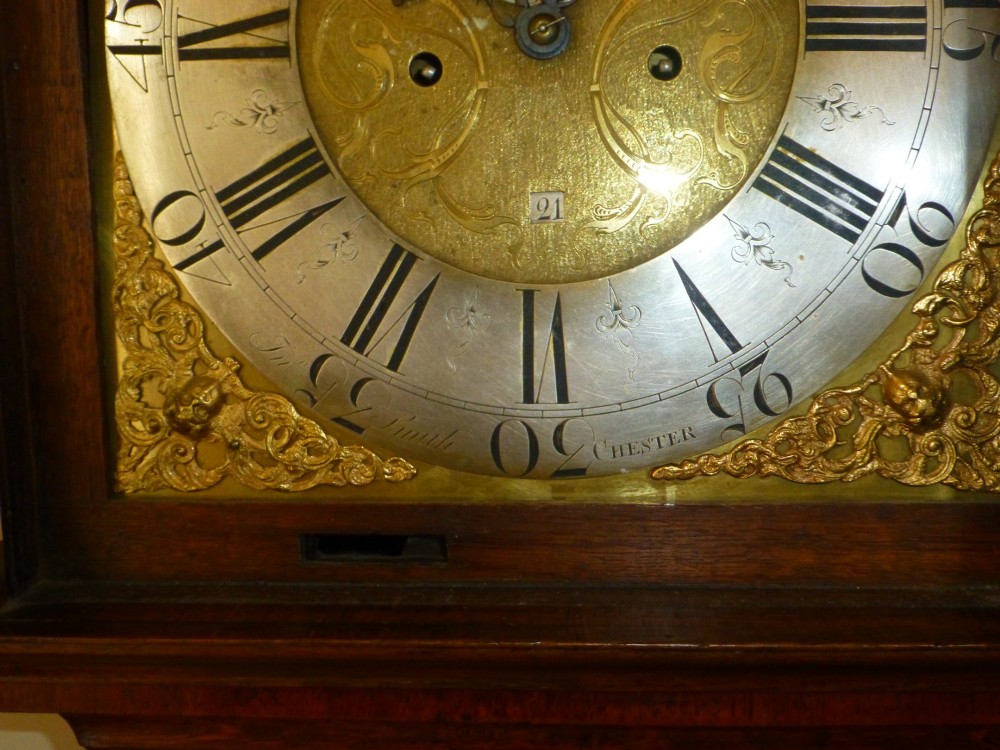 An eighteenth-century oak and walnut longcase clock featuring a square brass dial, decorative brass finials, and a slender veneered trunk door. View VI