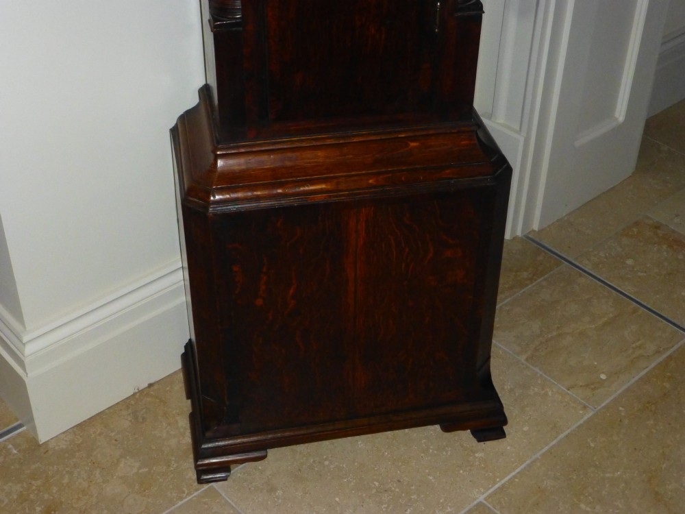 An eighteenth-century dark oak and walnut longcase clock featuring a square brass dial, turned columns, and a hood with a moulded cornice. View II