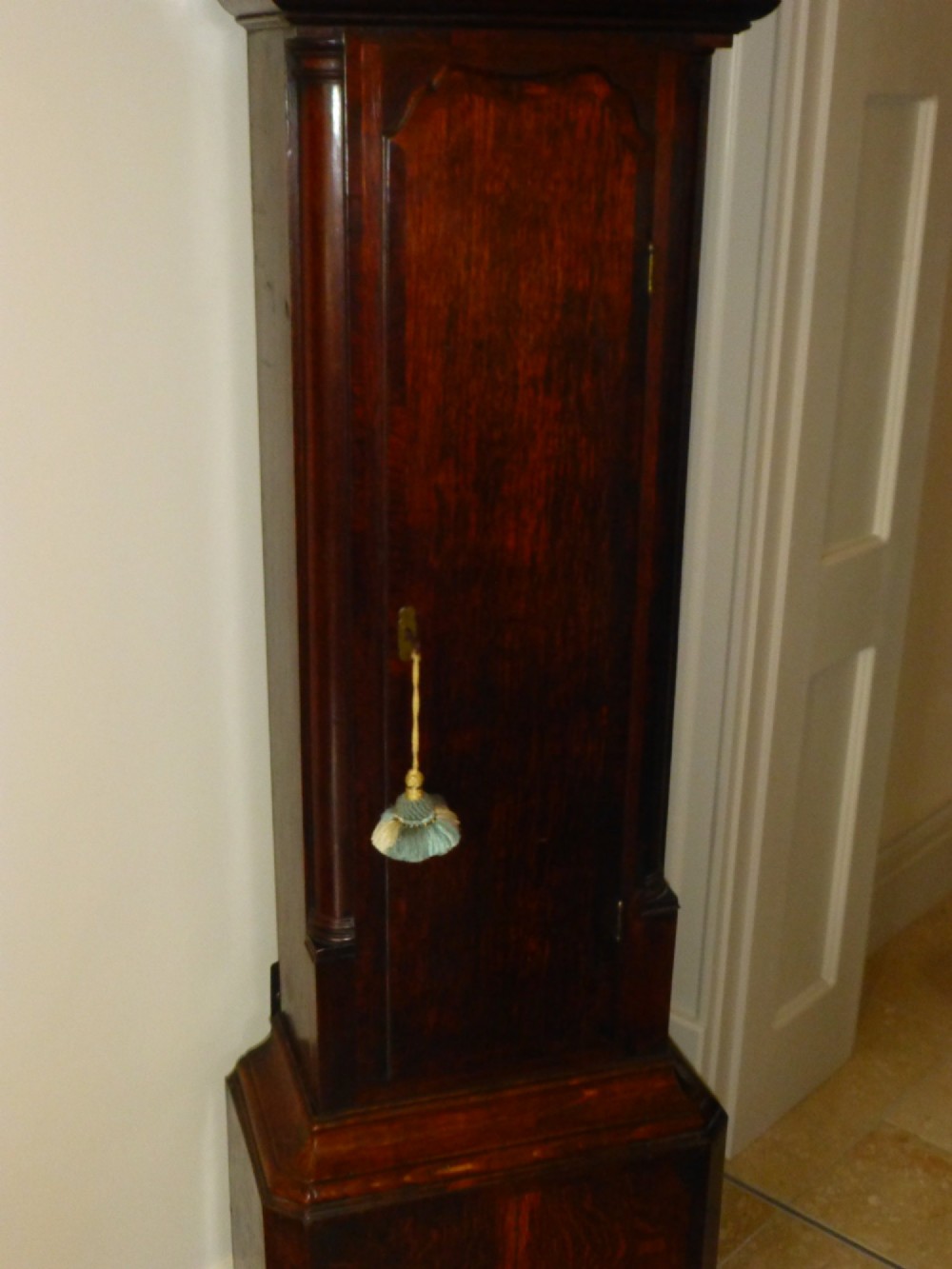 An eighteenth-century dark oak and walnut longcase clock featuring a square brass dial, turned columns, and a hood with a moulded cornice. View V