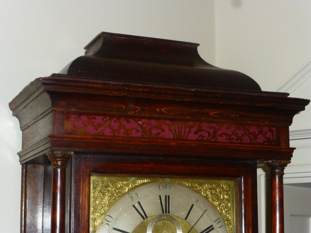An eighteenth-century dark oak and walnut longcase clock featuring a square brass dial, turned columns, and a hood with a moulded cornice. View VI