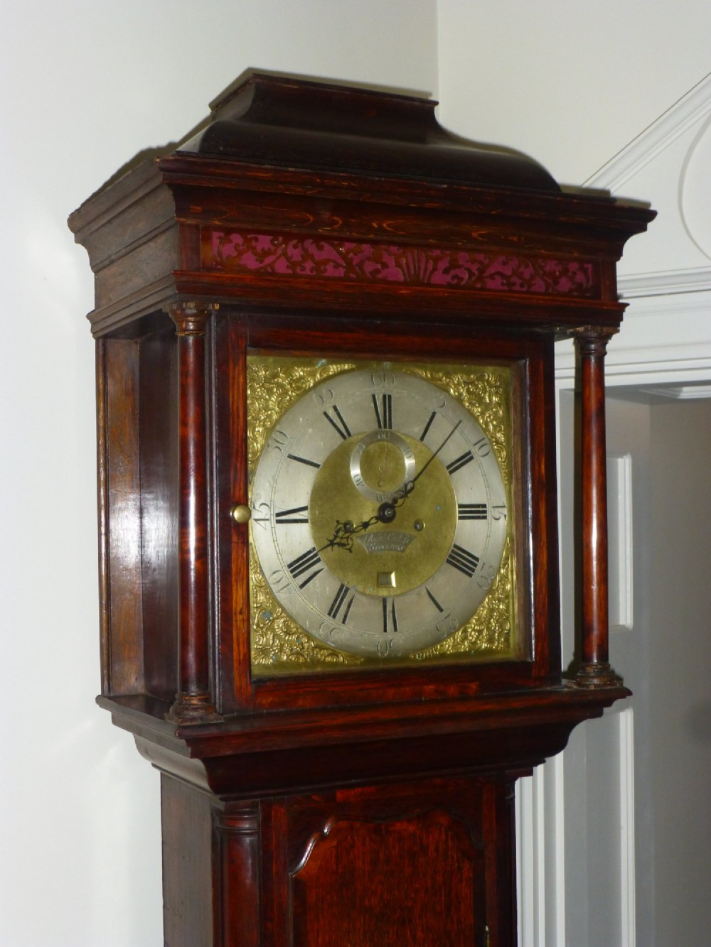 An eighteenth-century dark oak and walnut longcase clock featuring a square brass dial, turned columns, and a hood with a moulded cornice. View VII