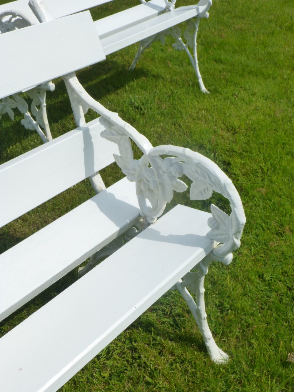A set of four white painted Victorian garden benches with cast iron end frames in a blackberry and leaf pattern and wooden slatted seats. View III