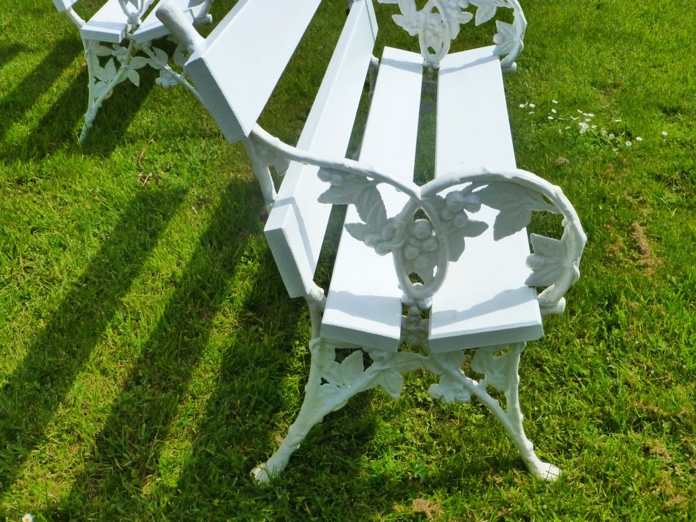 A set of four white painted Victorian garden benches with cast iron end frames in a blackberry and leaf pattern and wooden slatted seats. View V