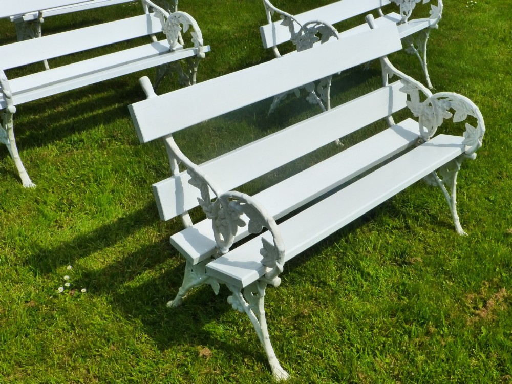 A set of four white painted Victorian garden benches with cast iron end frames in a blackberry and leaf pattern and wooden slatted seats. View VI
