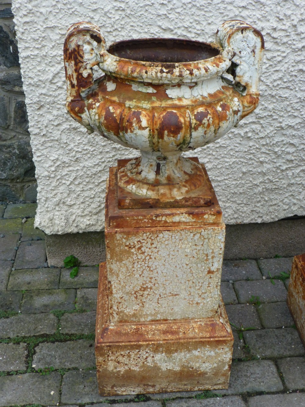 A pair of Regency period cast iron campana urns with scrolled handles, displaying distressed off-white paint and surface rust, mounted on square cast iron pedestals. View II