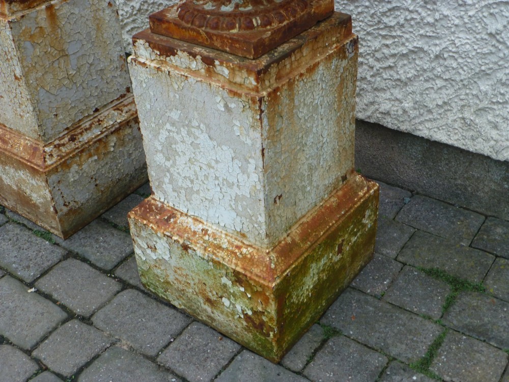 A pair of Regency period cast iron campana urns with scrolled handles, displaying distressed off-white paint and surface rust, mounted on square cast iron pedestals. View VI