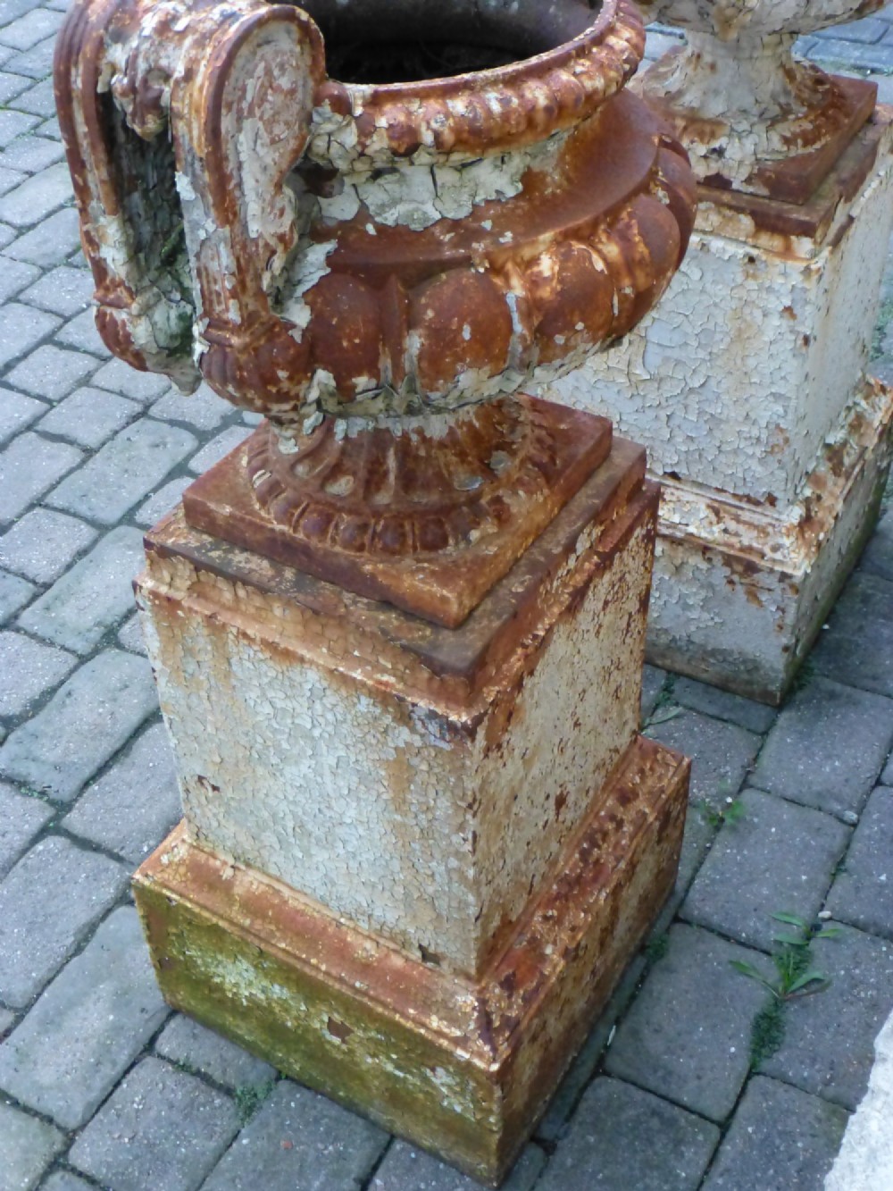 A pair of Regency period cast iron campana urns with scrolled handles, displaying distressed off-white paint and surface rust, mounted on square cast iron pedestals. View VIII