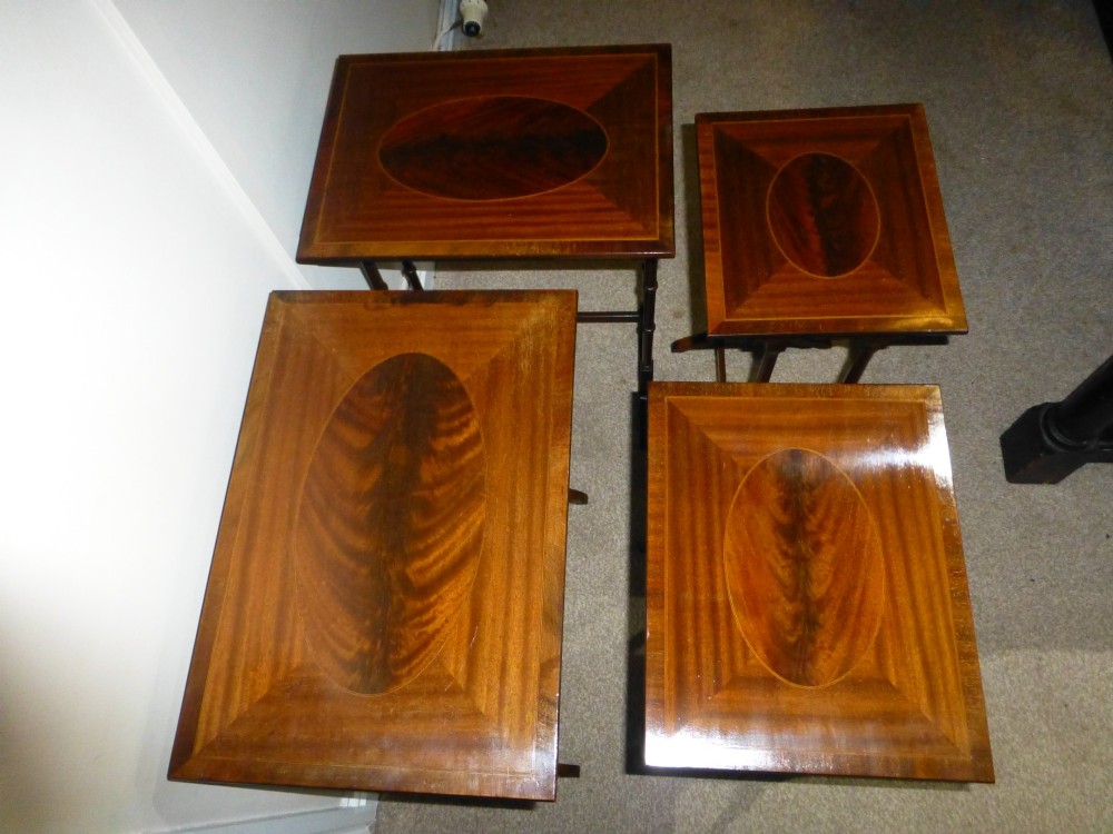 A set of four graduated mahogany nesting tables featuring oval inlay motifs and turned wooden legs, stacked in a cascading arrangement. View IV