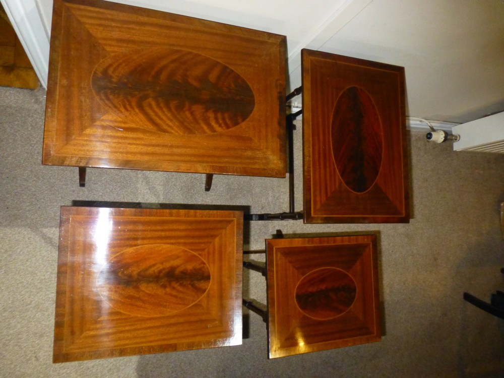 A set of four graduated mahogany nesting tables featuring oval inlay motifs and turned wooden legs, stacked in a cascading arrangement. View V