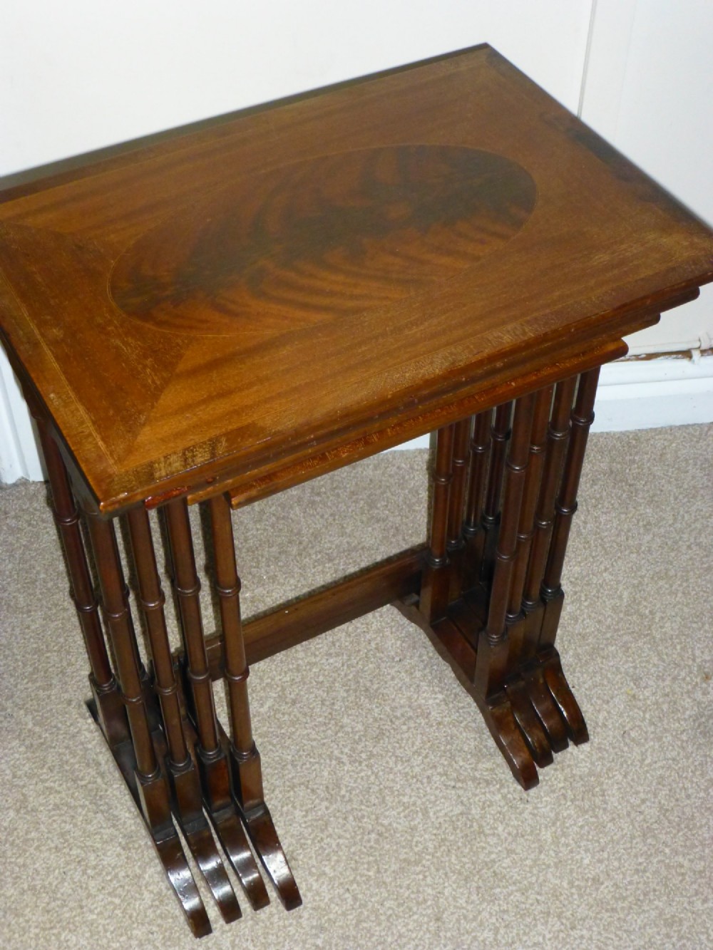 A set of four graduated mahogany nesting tables featuring oval inlay motifs and turned wooden legs, stacked in a cascading arrangement. View VI