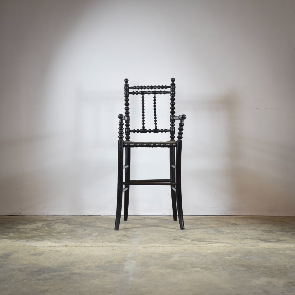 An antique ebonised childs high chair with bobbin-turned legs and backrest and a woven cane seat. View II