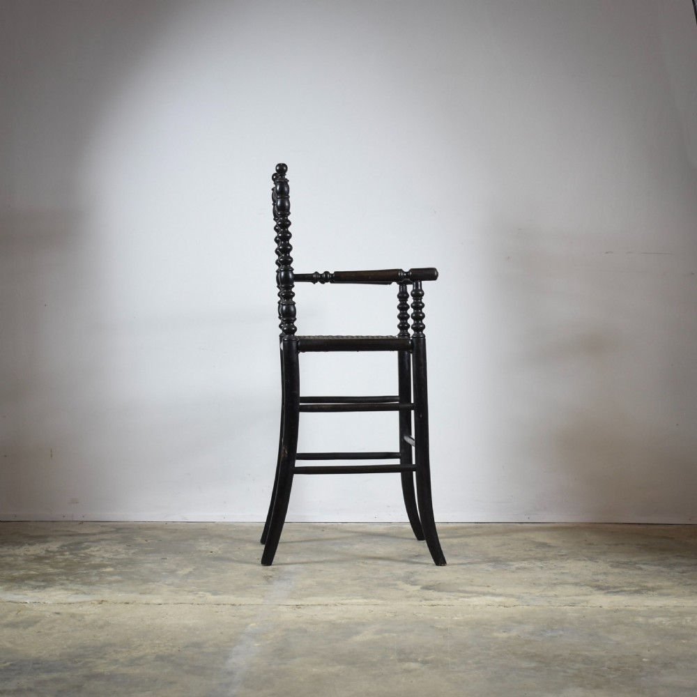 An antique ebonised childs high chair with bobbin-turned legs and backrest and a woven cane seat. View III