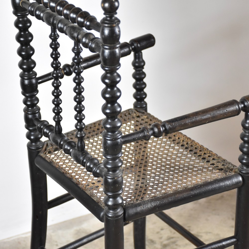 An antique ebonised childs high chair with bobbin-turned legs and backrest and a woven cane seat. View IV